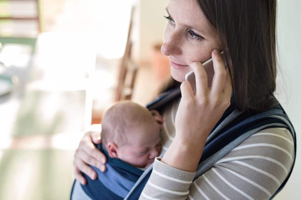 woman on cell phone with baby in carrier - when your bills exceed income
