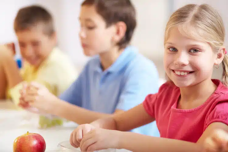 grupp av barn som har lunch under paus med fokus på leende tjej som tittar på kameran