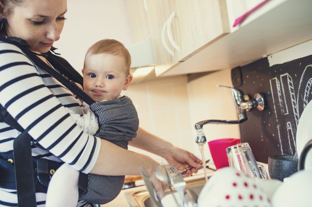 Mom with infant cleaning dishes at sink - infant hand me downs