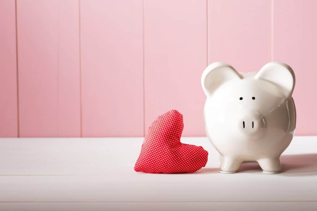 piggy bank next to red heart on white table top.