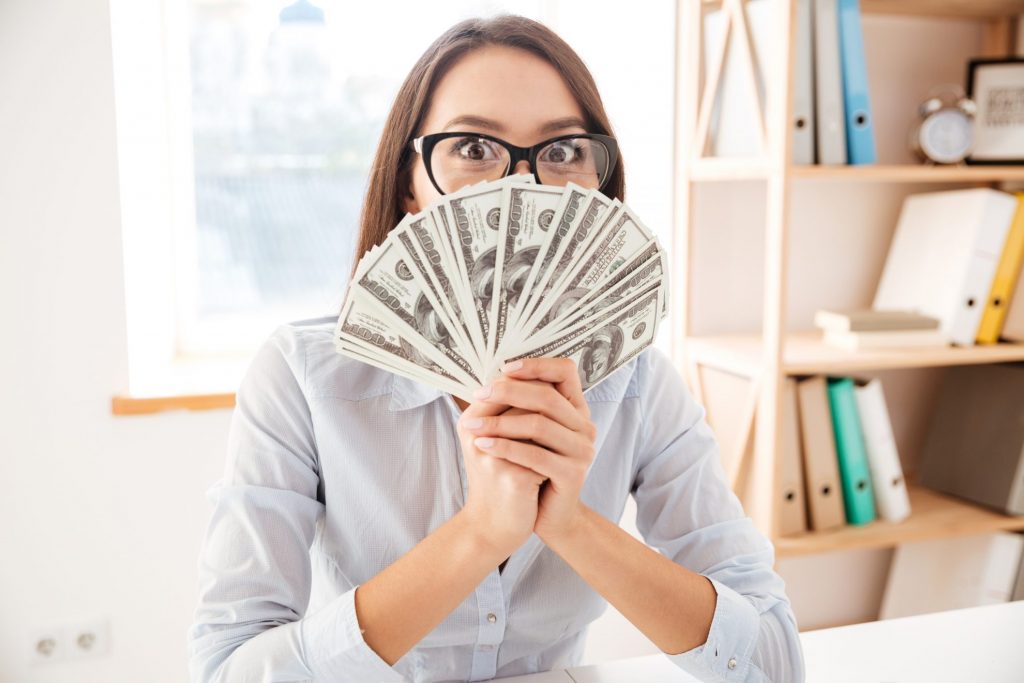 Businesswoman at desk hold money fanned out in hands - Smart Ideas To Take Control of Your Money