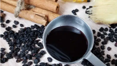 Homemade elderberry syrup in tablespoon next to loose elderberries