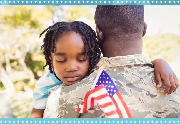 Military dad hold son with flag in hand.