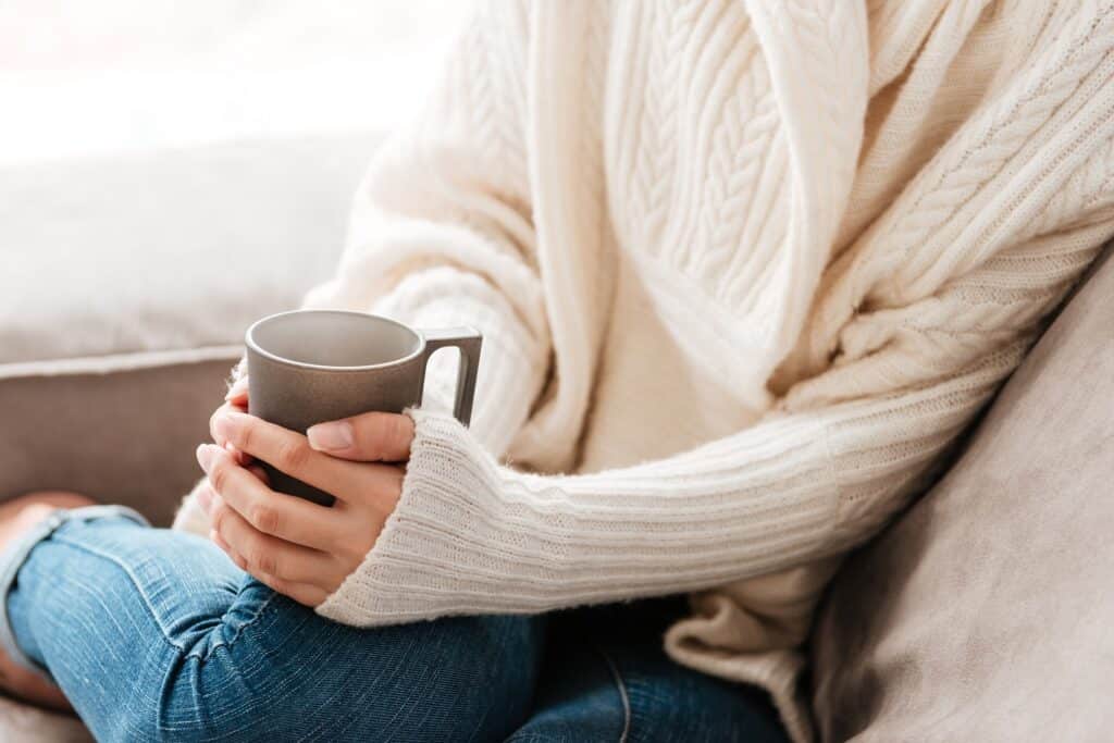Closeup of woman with cup of coffee sitting on sofa at home
