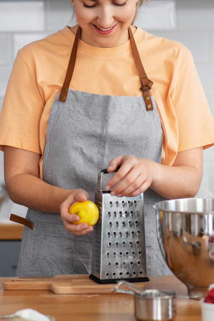 woman using cheese grater to grate lemon for zest