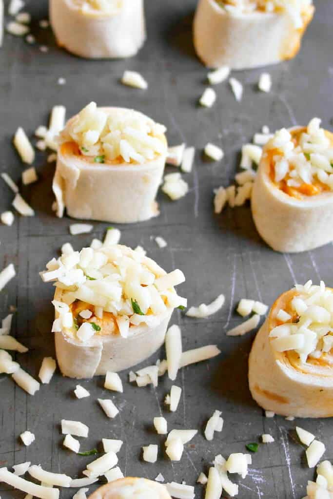 pinwheels with shredded cheese on top on baking pan