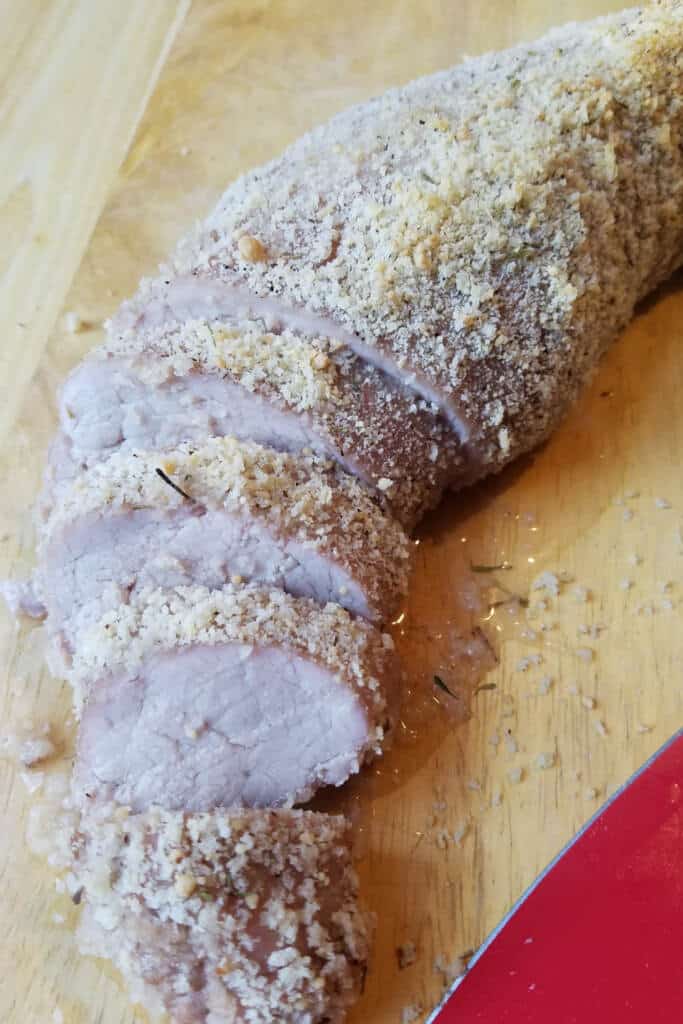 Cooked pork tenderloin on cutting board with red knife