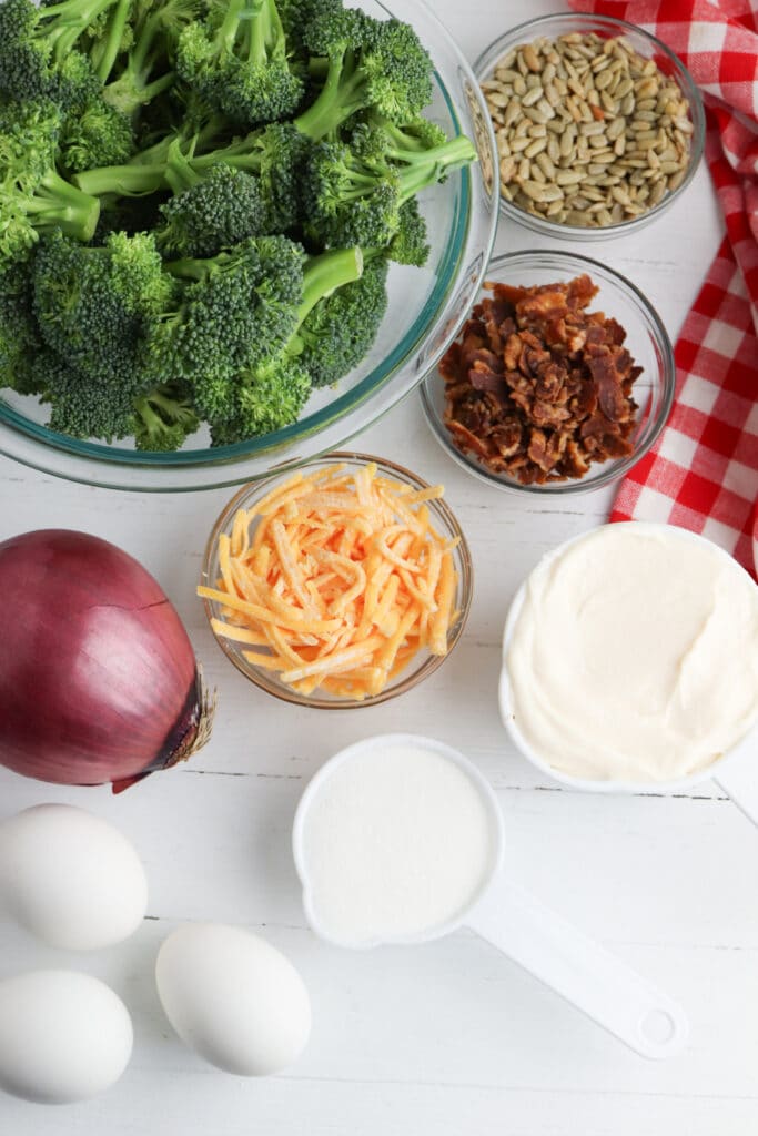 Ingredients for broccoli salad, pictured fresh broccoli, red onion, cheddar cheese shredded, bacon, sunflower seeds and mayonnaise