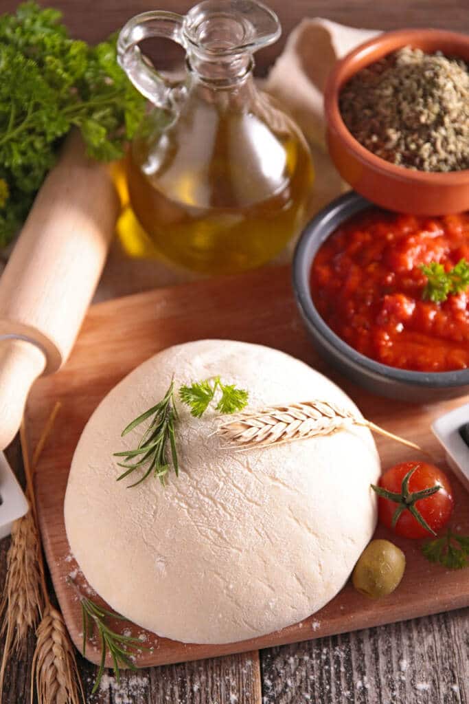 Pizza Dough on wooden cutting board with ingredients to make pizza