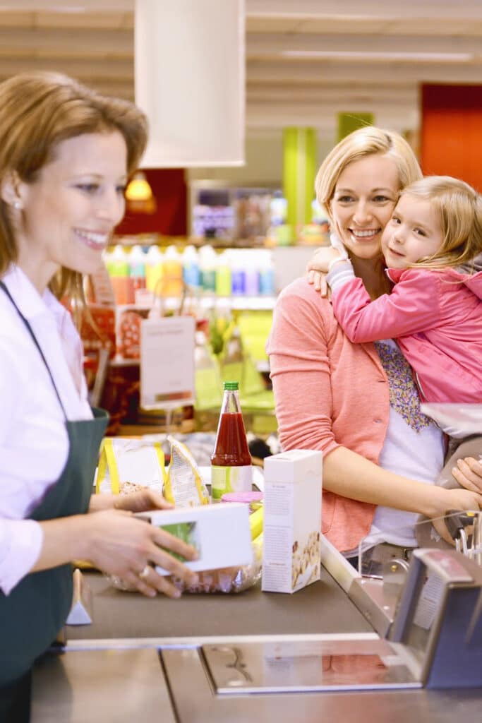 Using coupons at the grocery store "Woman holding small daughter at checkout register"