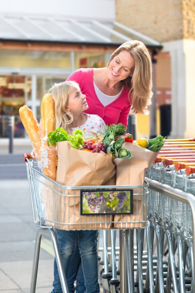 Woman and child with grocery cart leaving store with bags filled with groceries