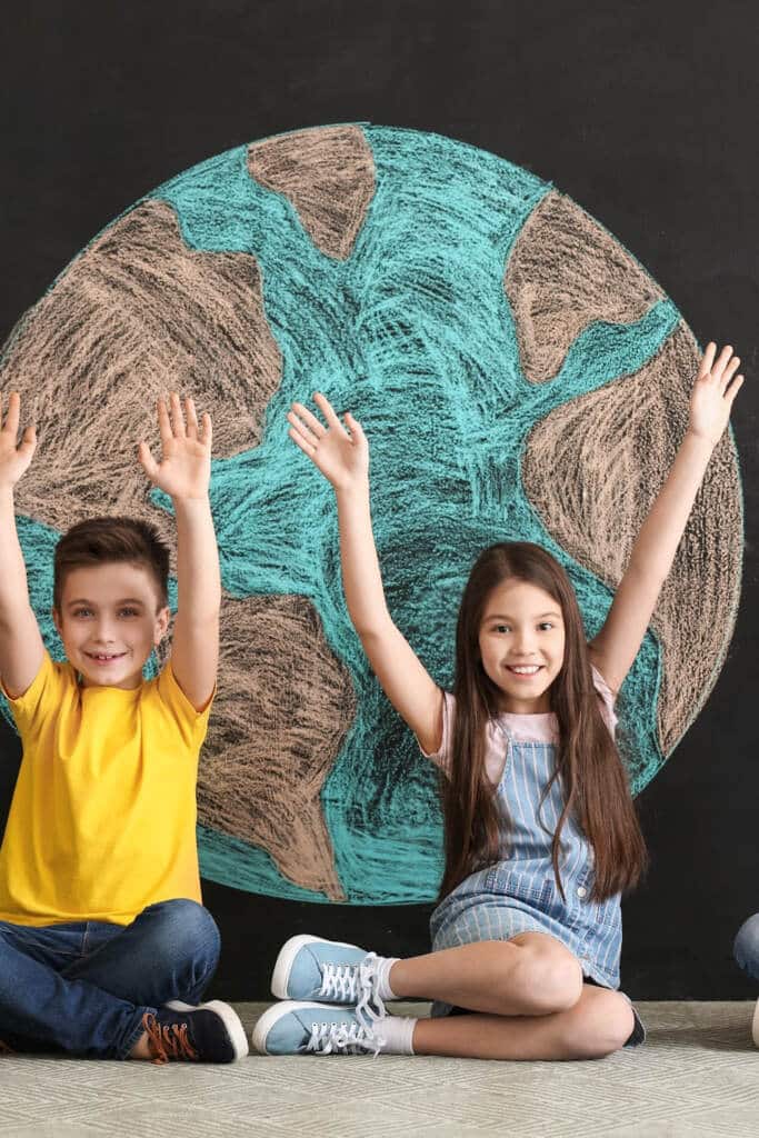 A boy and girl sitting with hands int he air in front of world map