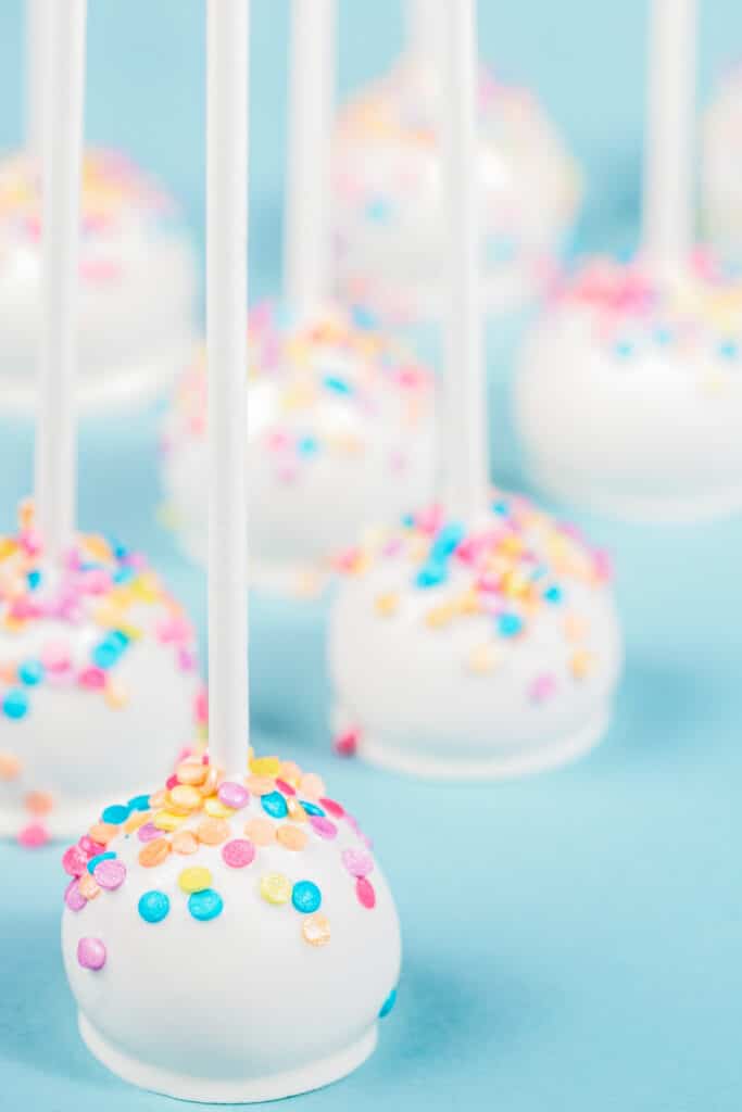 vanilla cheesecake cake pops on blue background with multicolored sprinkles