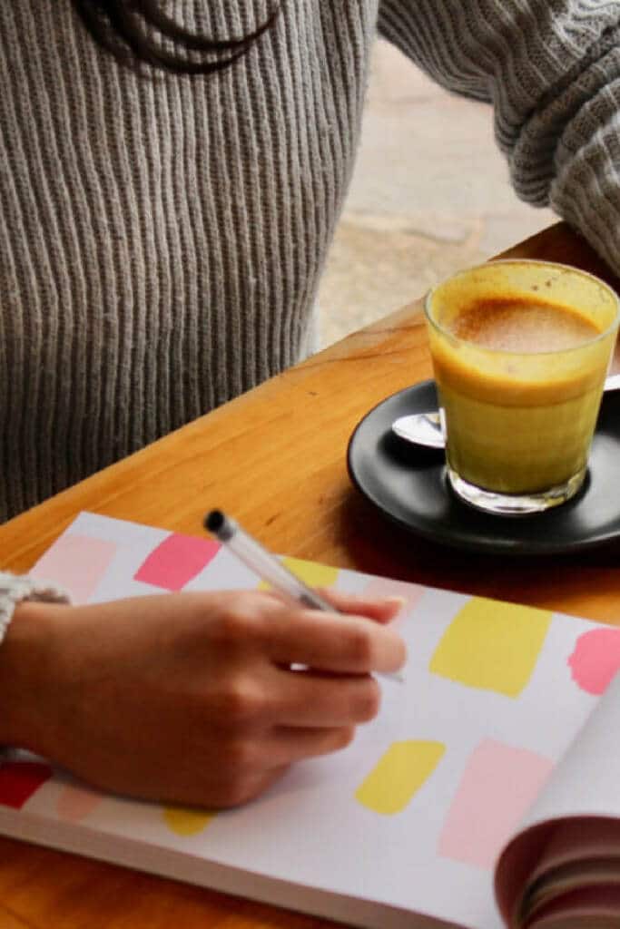 Woman sitting down at table with coffee writing out a meal planning list