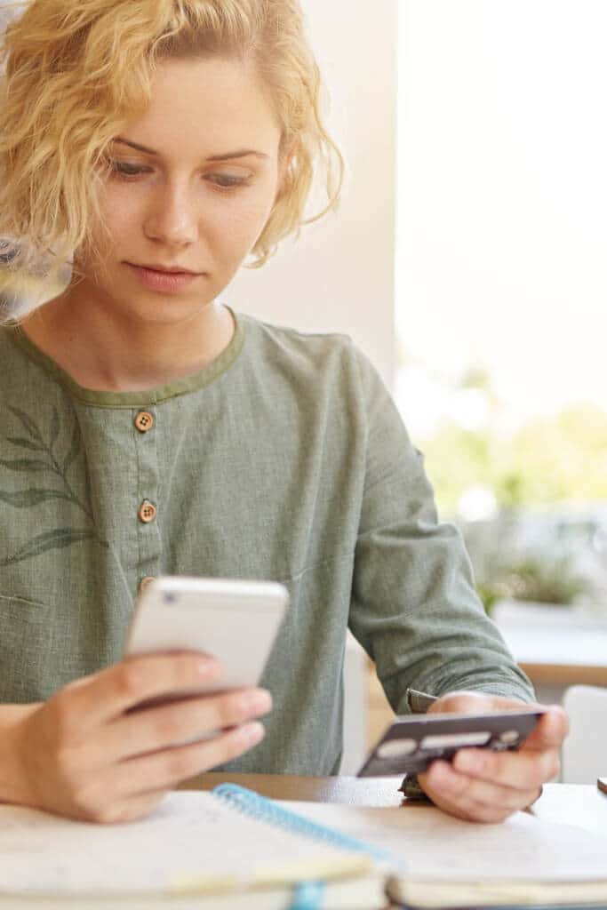 woman shopping online on phone with credit card in hand