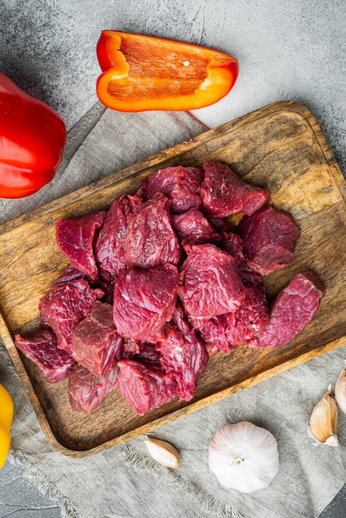 Stewed beef on dark wood cutting board with colored peppers