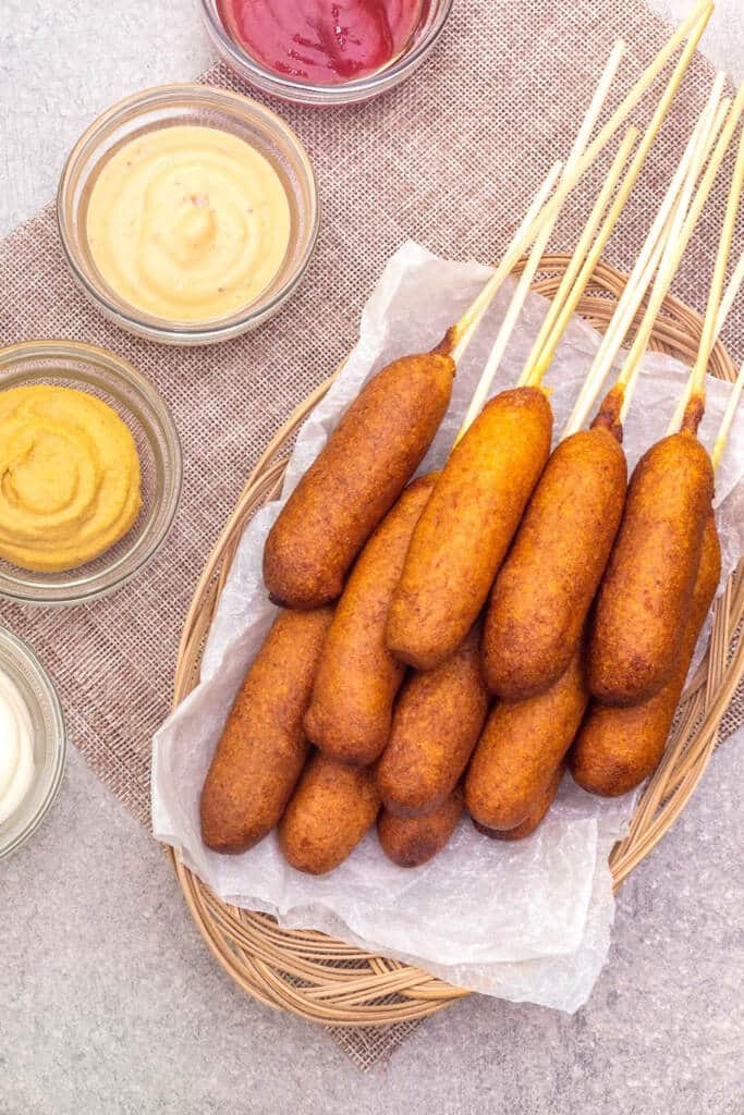 homemade corn dogs with three bowls of dipping sauce on Table