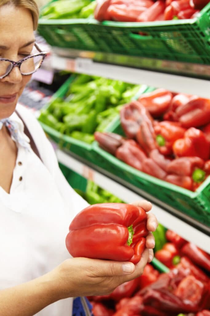 shop in season produce - woman holding red pepper in hand. Shopping in the produce section