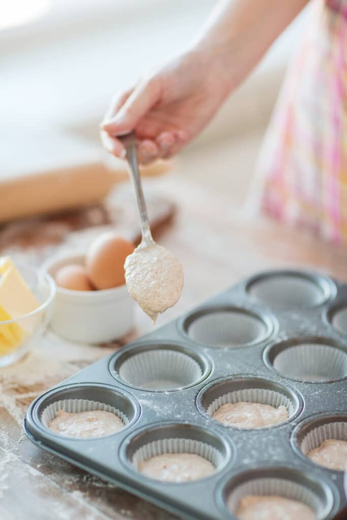 Filling cupcake tin with vanilla cupcake batter. Woman using spoon to fill cupcake pan
