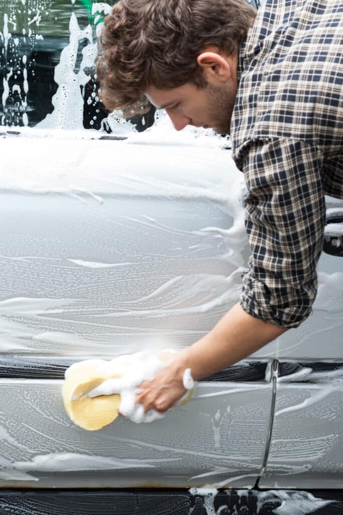 cleaning car exterior - man cleaning outside of car with soapy water and a sponge