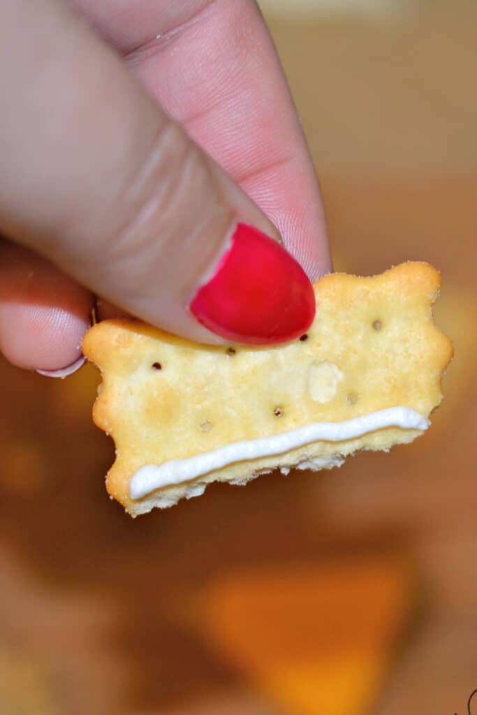 adding a line of whipped cream cheese to cracker