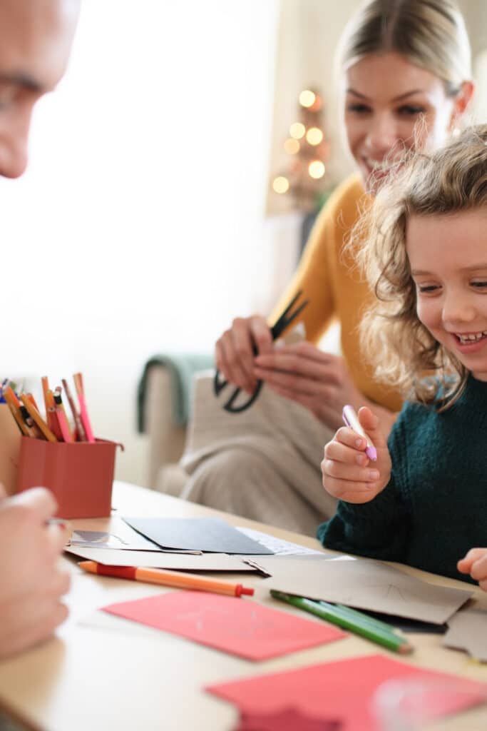family working on Christmas cards together on table