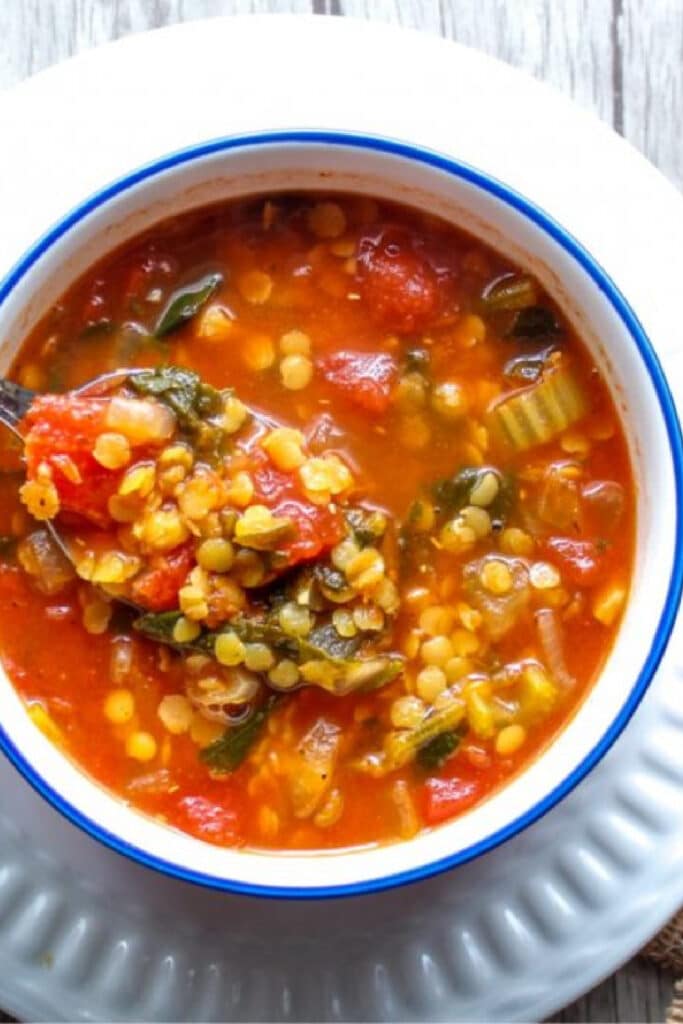 lentil soup in white bowl on white plate with spoon,