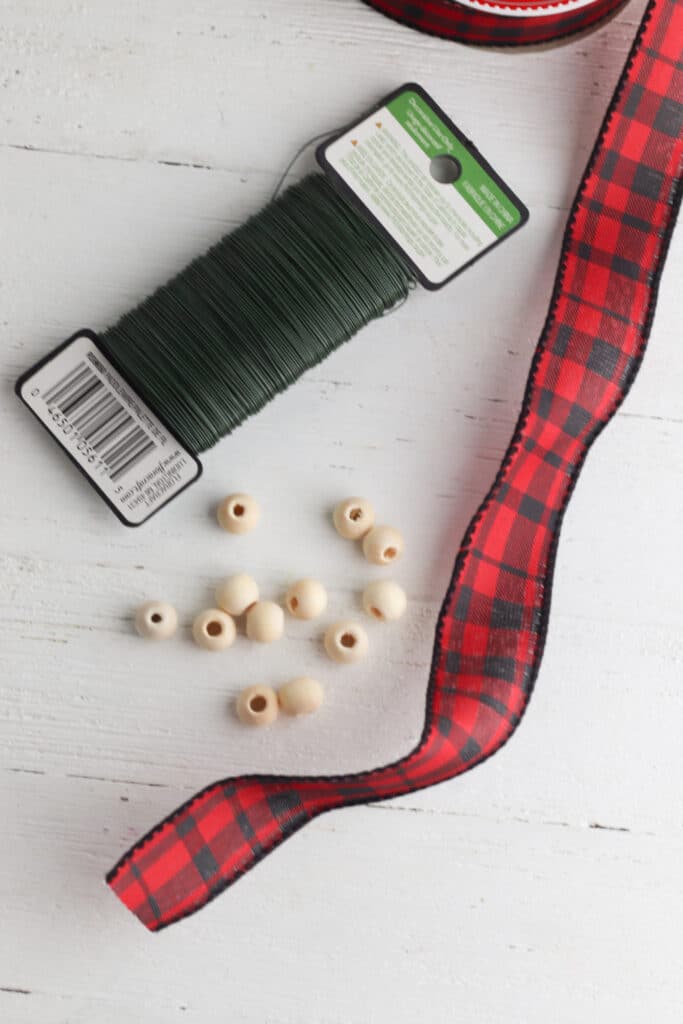 Items need to make homemade wood ornaments. Pictured wooden beads, wire and red ribbon