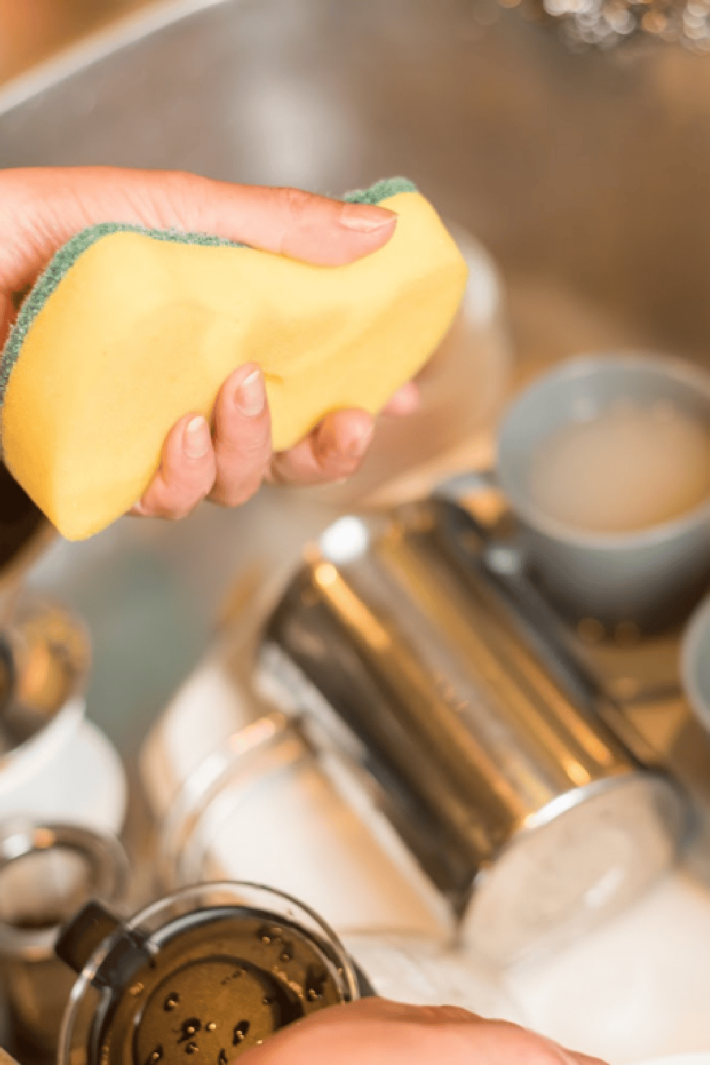 cleaning dishes in sink - close up on hand holding yellow sponge