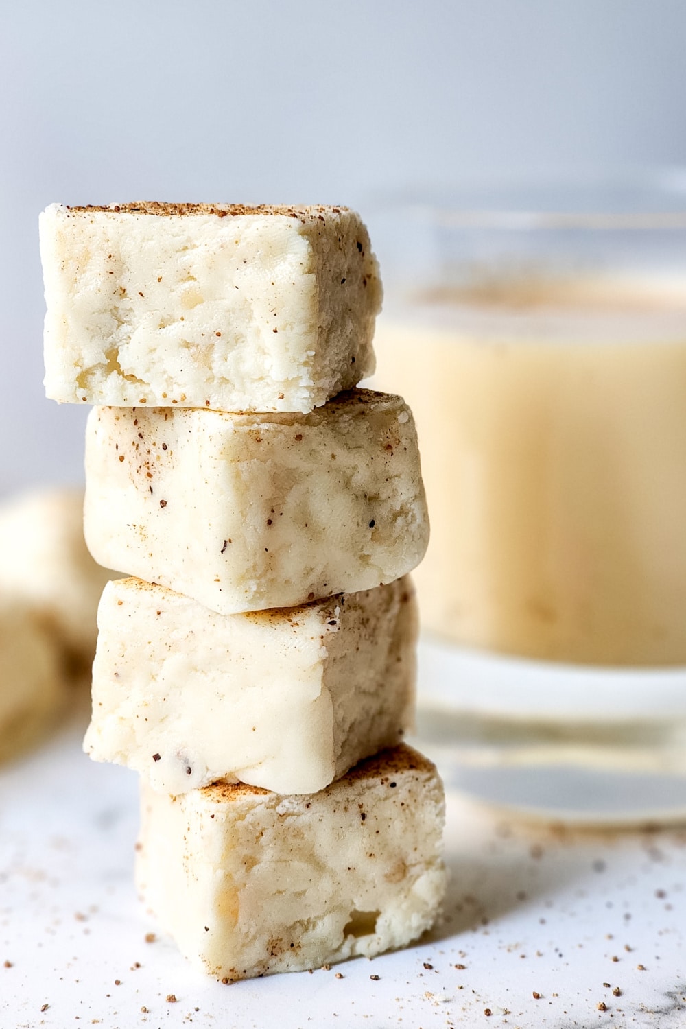 homemade white chocolate eggnog fudge - 4 stacked pieces pictured close up with sprinkles of cinnamon