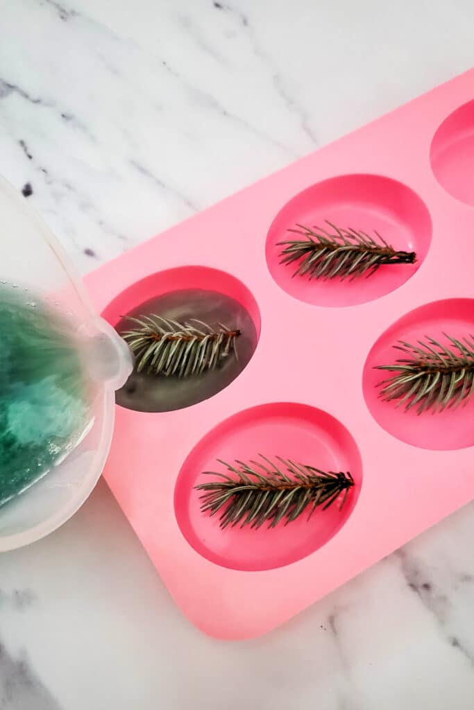 pouring soap mixture into molds with pine needle