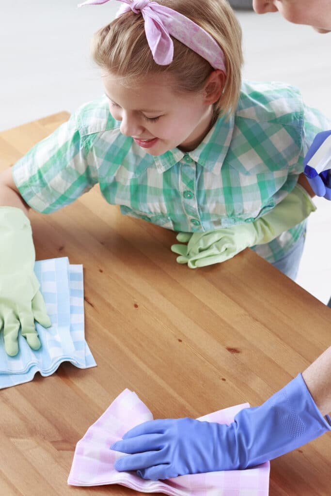teaching kids to clean - young child dusting ff table with rubber gloves on