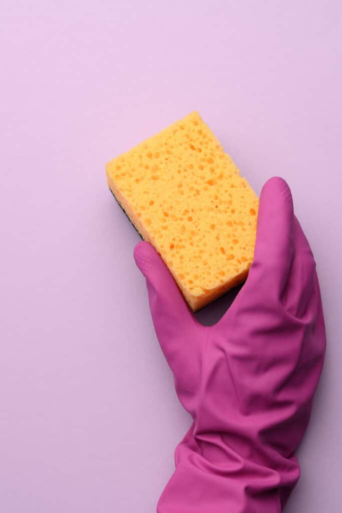 Cleaning your sponges - pictured hand in rubber glove holding yellow kitchen sponge