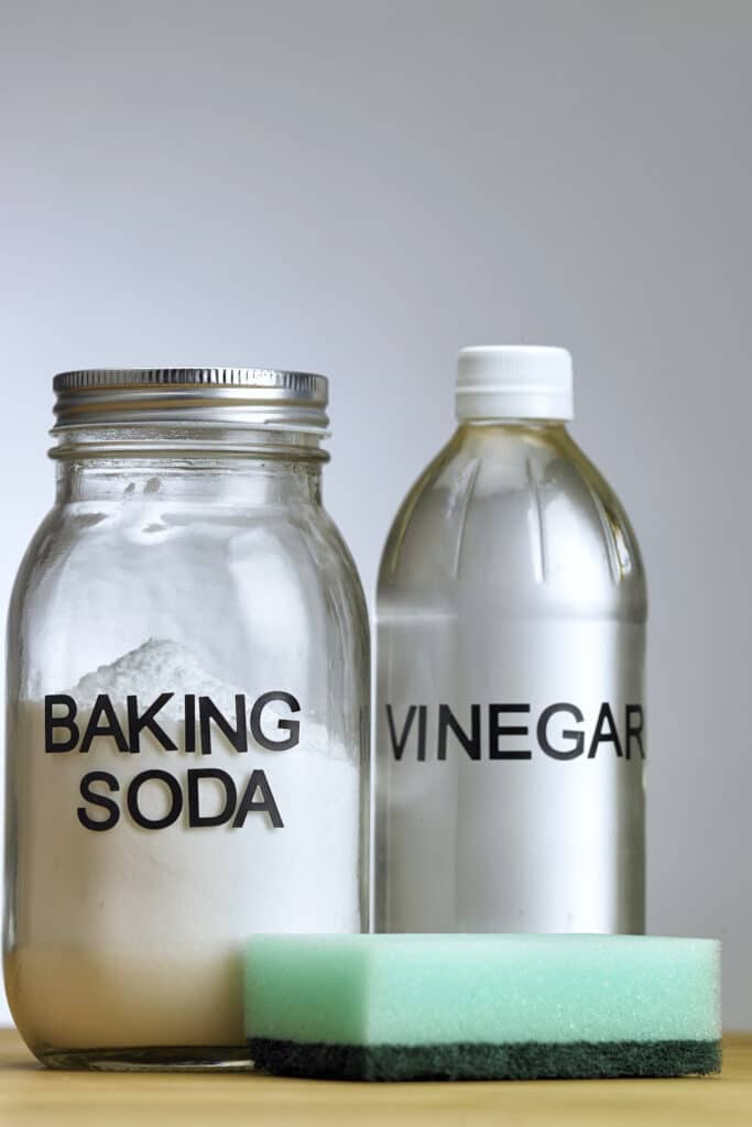 white vinegar and baking soda bottles next to a green sponge