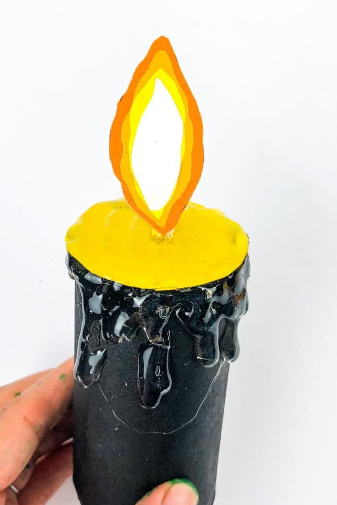 Adding hot glue to candle flame on top of painted black toilet paper tube