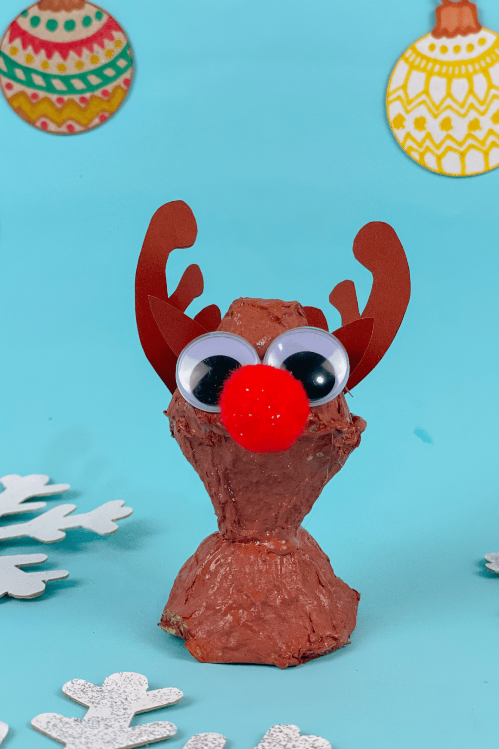 Completed Reindeer Egg Carton Craft on blue background with snowflakes