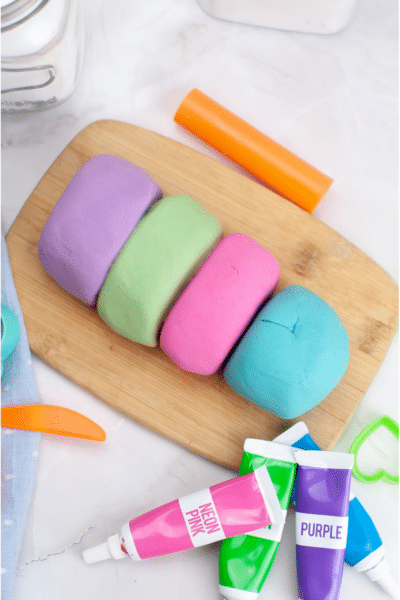 Homemade easy Play Dough Recipe 4 different colours of play dough on wooden cutting board