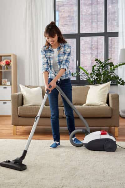woman using vacuum cleaning on rug in living room healthy cleaning