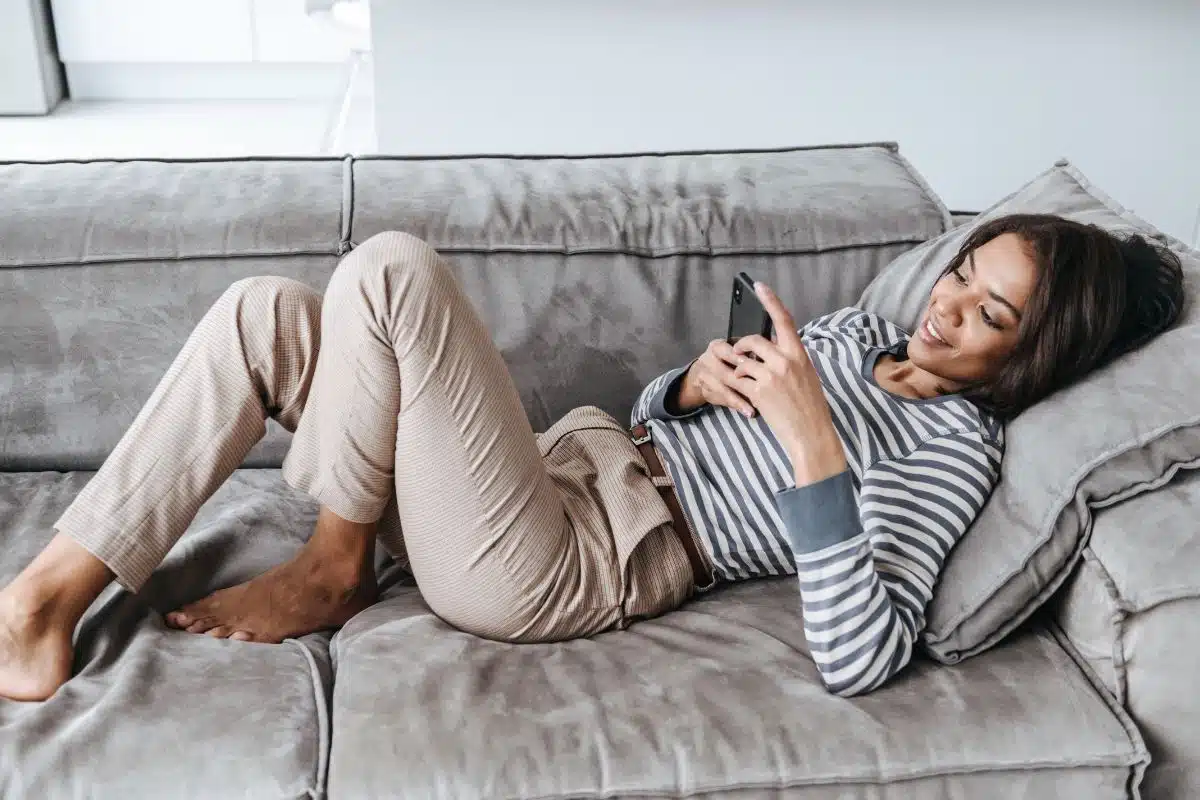 Woman sitting on couch phone comfy clothes Photo Credit Canva Pro Stock Image